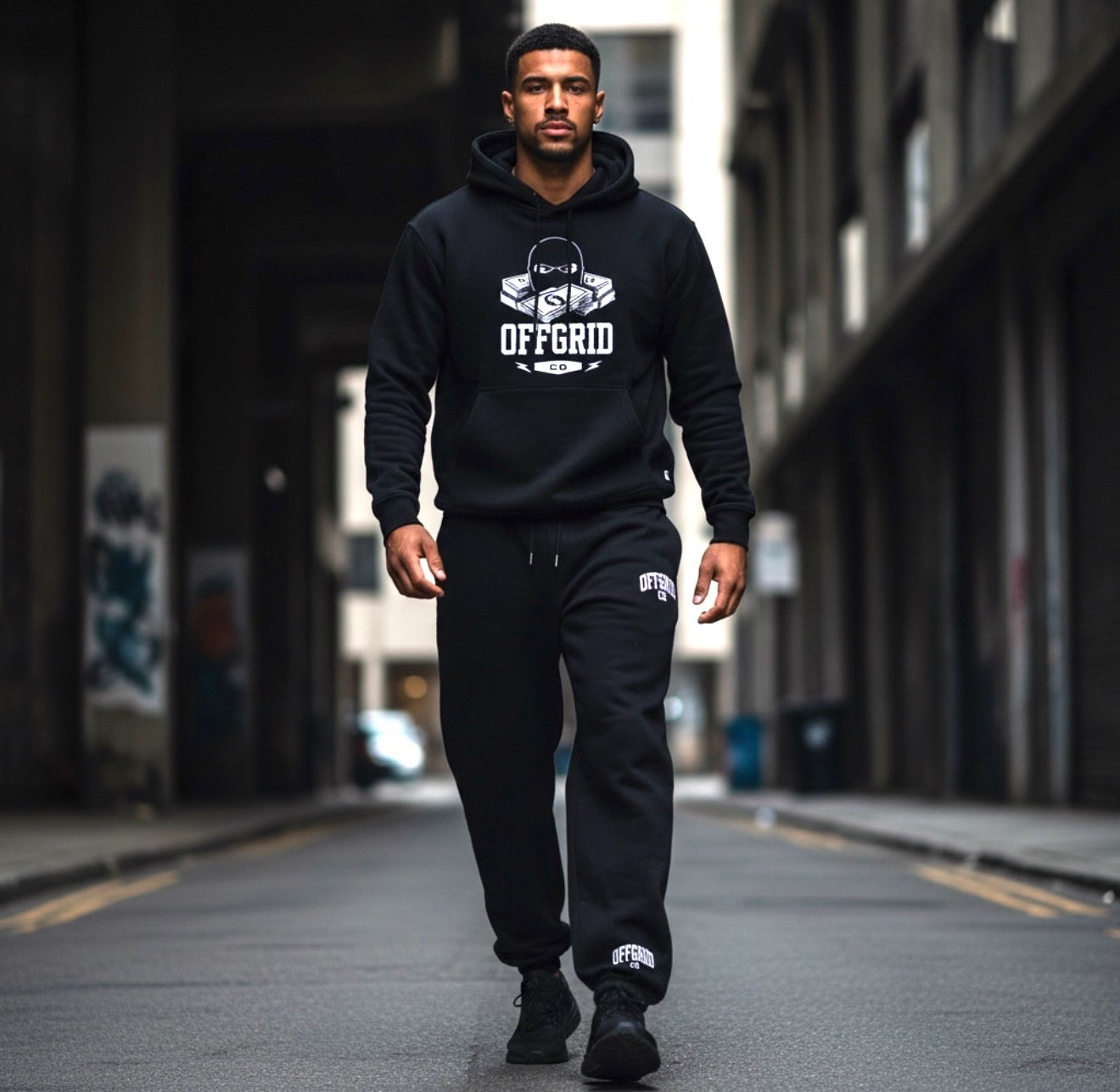 Man wearing a black 'OFFGRID' hoodie and pants walking down an urban street.